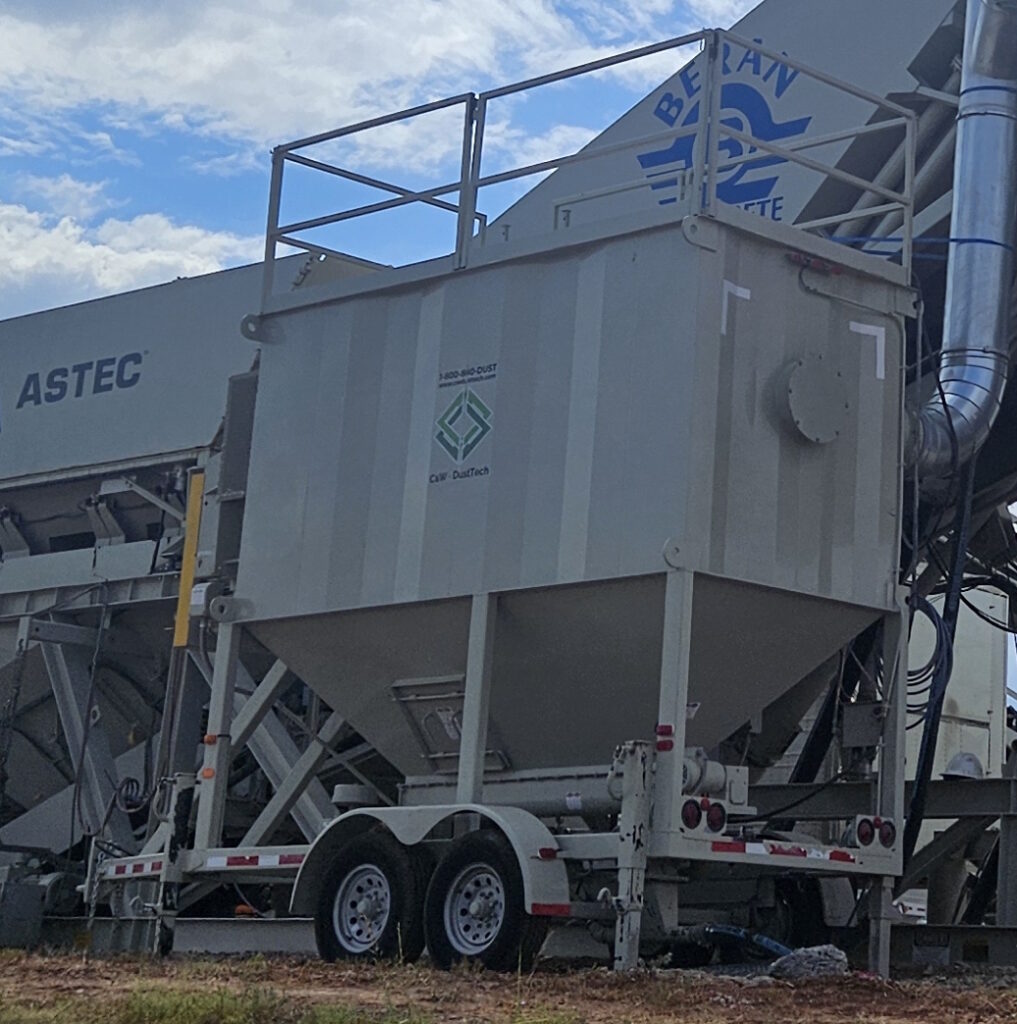 A large industrial C&W CP2100M Central Dust Collector on a trailer is parked outdoors, labeled with ASTEC logos, under a partly cloudy sky. Piping and machinery are attached to the structure.