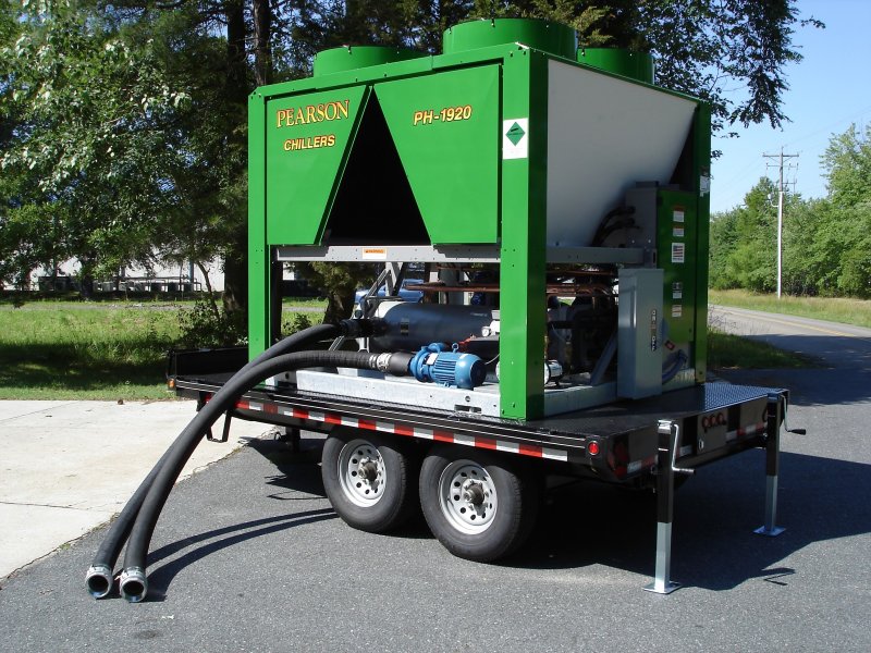 A large water chiller unit for concrete plants labeled Pearson Chillers PH-1920 is mounted on a flatbed trailer with hoses attached, parked outdoors near grass and trees on a sunny day.