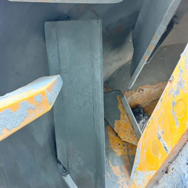 Close-up view of the inside of an industrial machine with worn metal blades and yellow-painted, chipped surfaces, showing signs of use and abrasion.